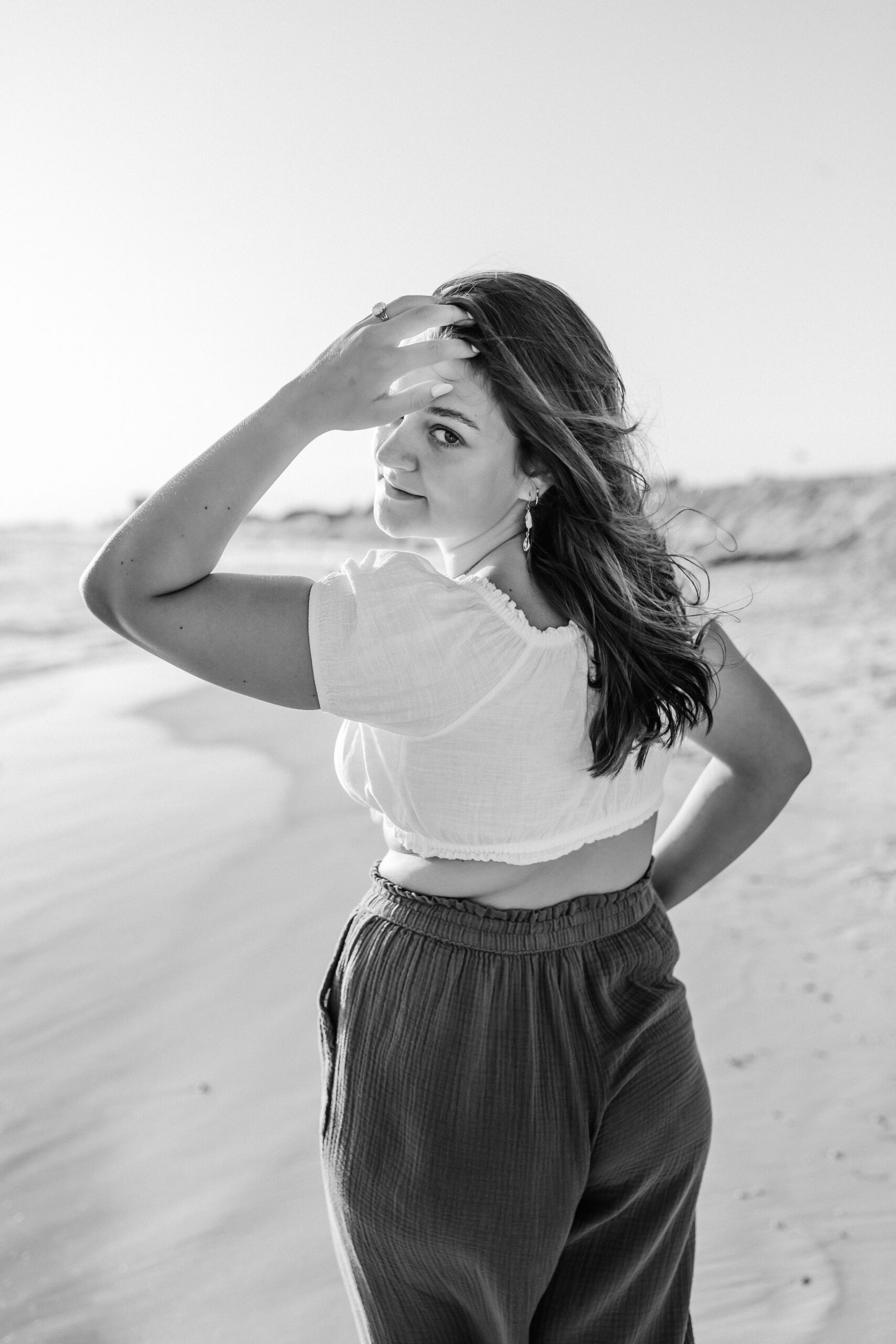 Senior girl looking back at camera running fingers through hair - graduation portraits in St. Andrews State Park by Brittney Stanley with Be Seen Photos