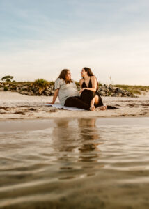 Young lesbian couple snuggles and chats on beach in PCB Fl - portrait taken at sunrise by Brittney Stanley of Be Seen Photos
