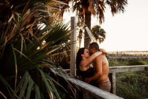 Young couple kisses & embraces under boardwalk shower in St. Andrews State Park - image taken at sunrise by Brittney Stanley of Be Seen Photos
