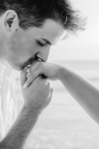 Newly engaged young man kisses bride to be's hand & engagement ring - on beach of PCB Florida