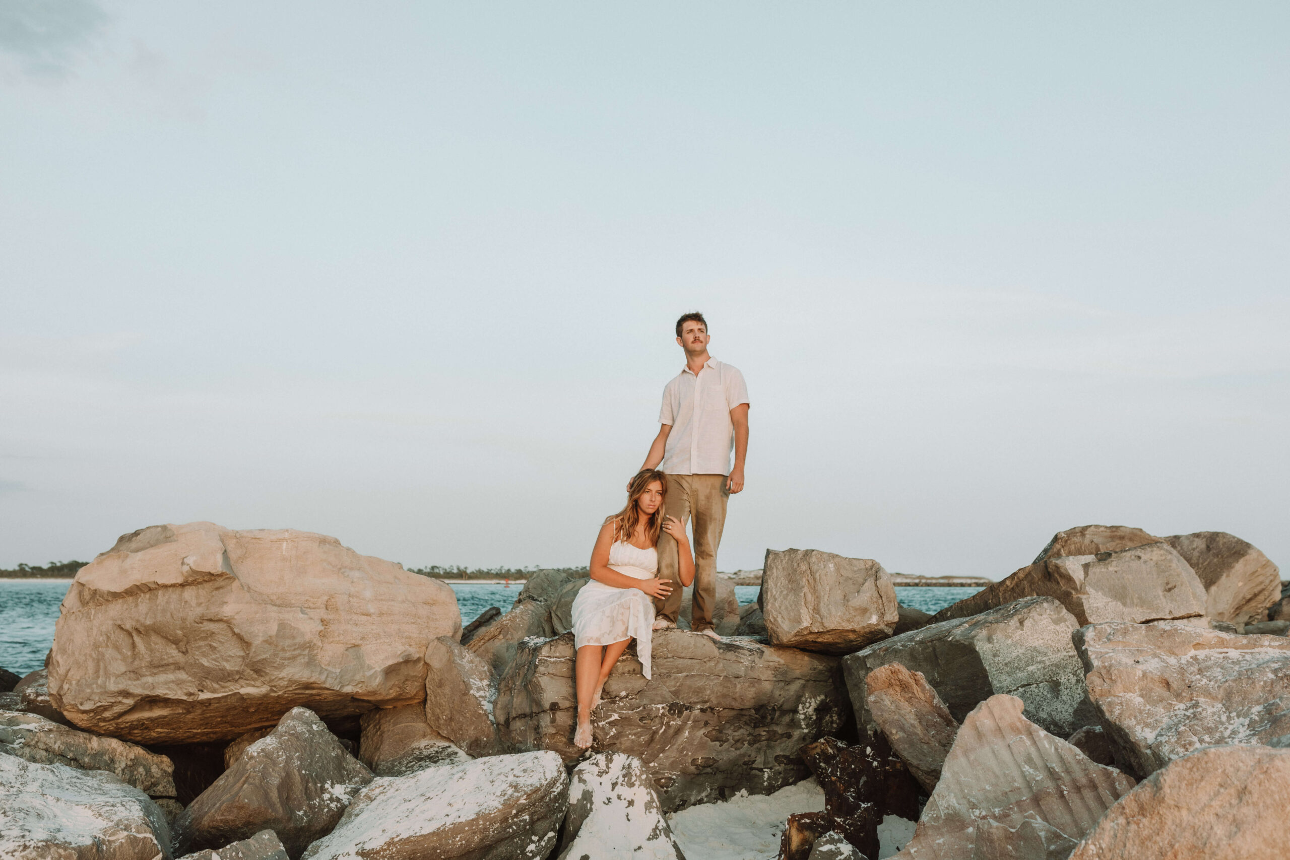 Newly engaged young couple pose on rocks at sunset on beach in PCB Florida
