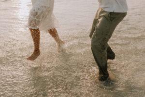 newly engaged young couple wearing white & tan play in water beachside in PCB Florida