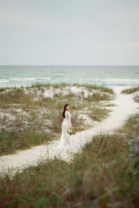 Bride posing regally on sand path in West PCB, Florida - she's wearing gown & holding flowers