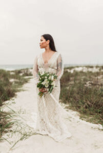 Bride posing regally on sand path in West PCB, Florida - she's wearing gown & holding flowers