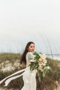 Bride posing regally on sand path in West PCB, Florida - she's wearing gown & holding flowers towards the camera