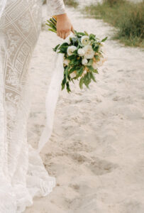 Bride walking down beach path in West PCB, Florida - wearing gown & holding flowers.  Image taken by panama city wedding photographer Brittney Stanley